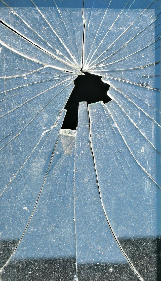 Cracked glass window with a large hole, spiderweb cracks, and blue sky behind it