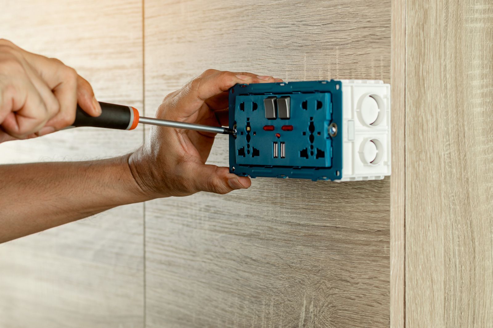Person using a screwdriver to install an electrical outlet on a wooden wall.