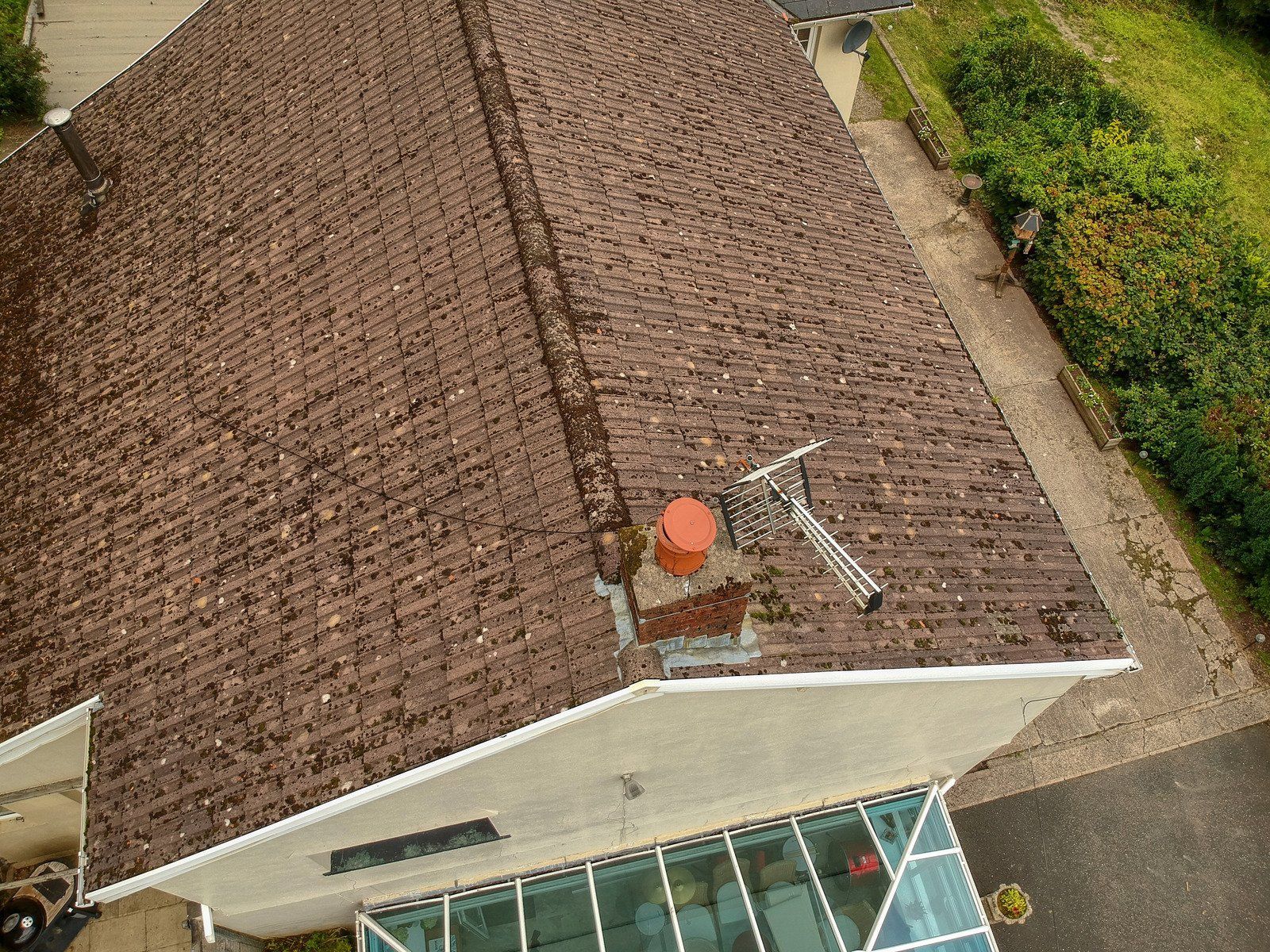 Brown-shingled roof with a chimney and ladder. A section of a white house and a glass-roofed structure are visible.