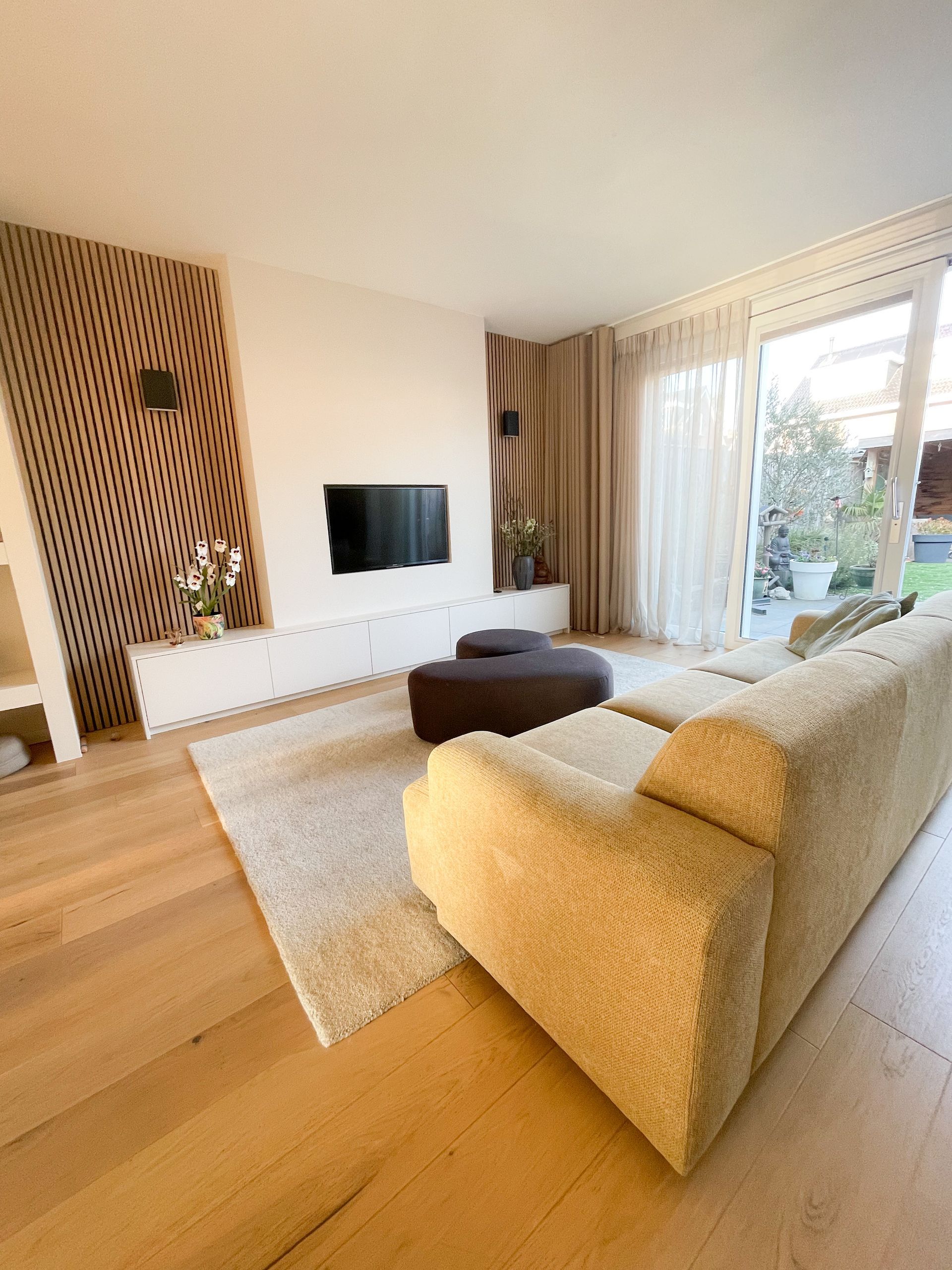Een minimalistisch ingerichte woonkamer met een geel/groene bank voor een op maat gemaakt en ontworpen wandmeubel waar de televisie in geïntegreerd is. 