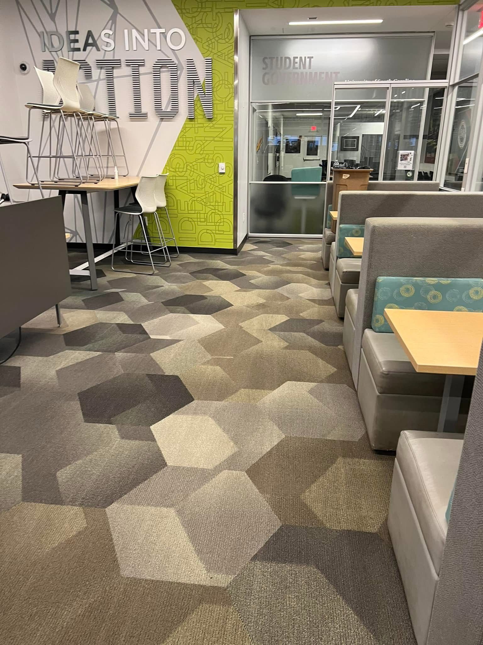 A library seating area with booths, tables, and patterned carpet. Green and white 