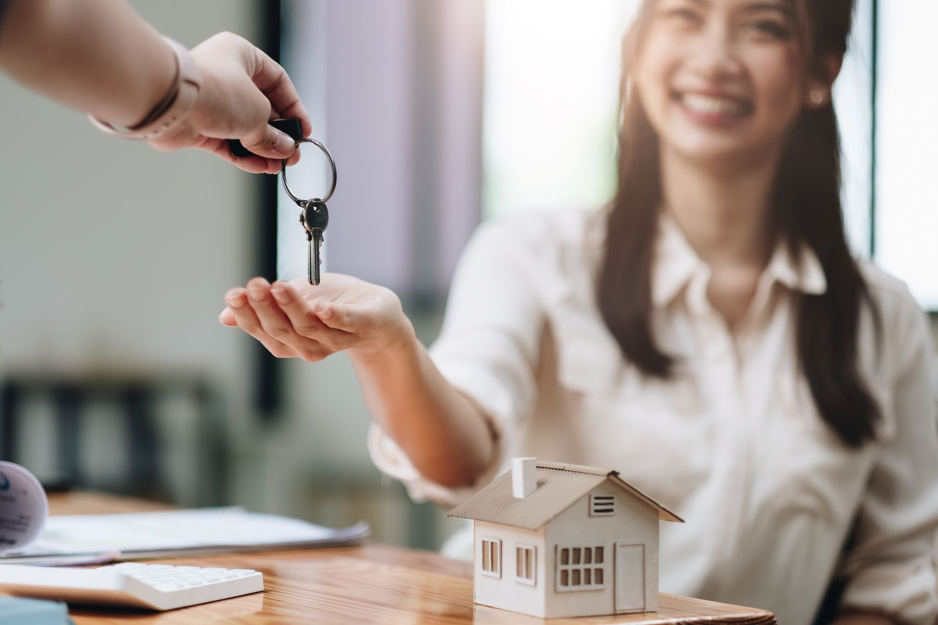 A woman is sitting at a table receiving keys from a real estate agent.