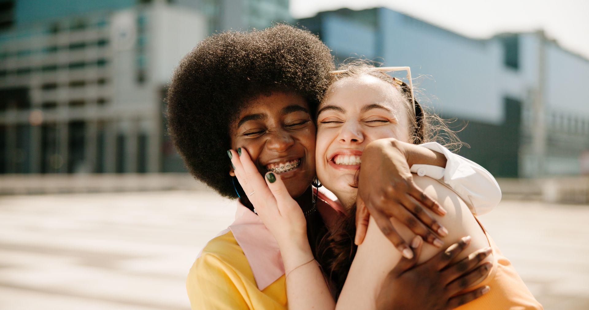 Two women are hugging each other and smiling in front of a building.