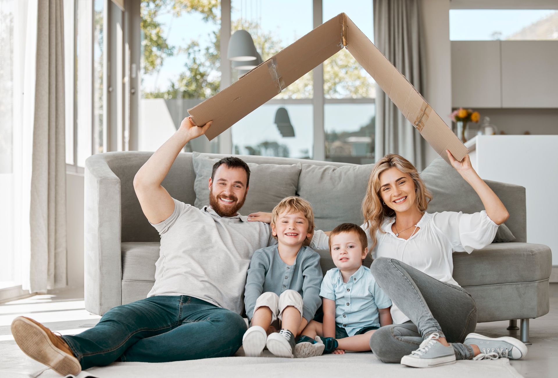 A family is sitting on the floor in a living room holding a cardboard house.
