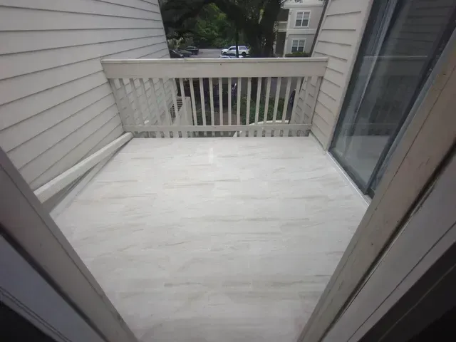 Empty white balcony with railing, siding, and sliding glass door overlooking nearby buildings
