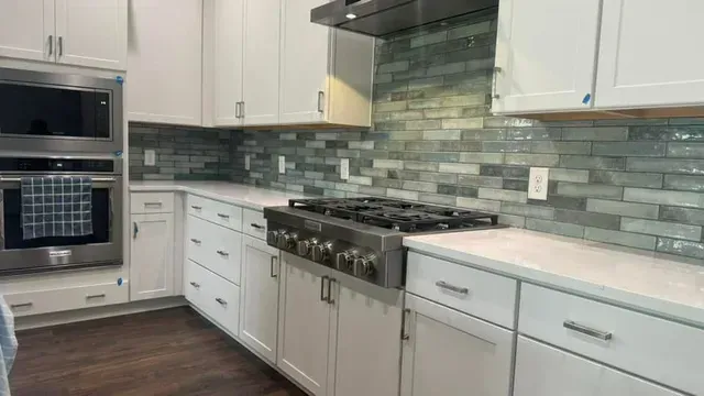 Modern kitchen with white cabinets, gray tile backsplash, stainless steel appliances, and dark wood flooring