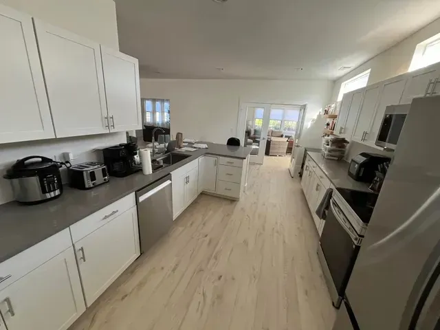 Bright, modern galley kitchen with white cabinets, stainless appliances, and light wood flooring.