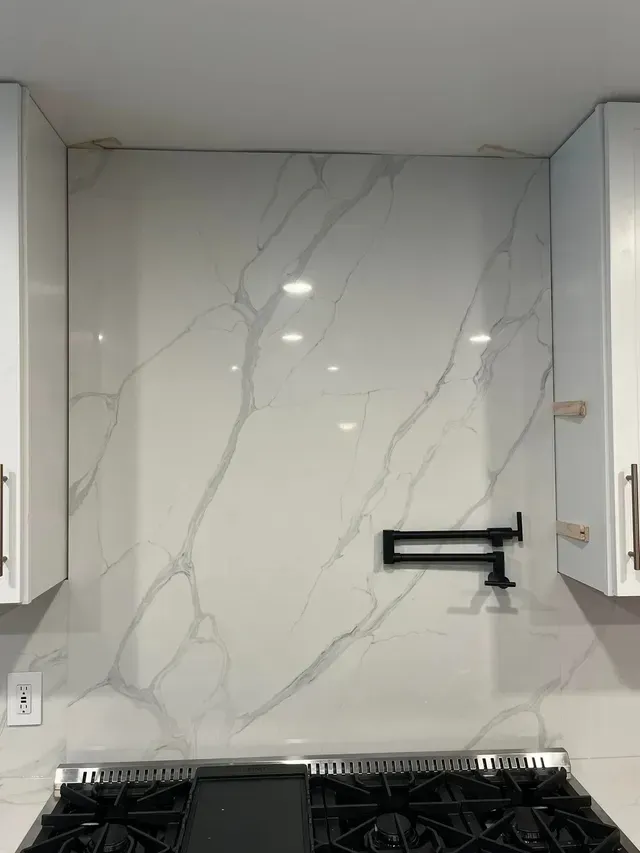 White marble-look kitchen backsplash with black pot-filler above stove and white cabinets on both sides