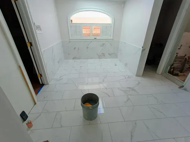 Partially tiled bathroom under renovation with a bucket on the floor and a window at the far end