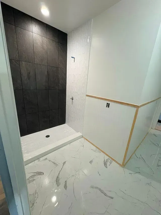 Modern bathroom with black shower wall, white tile floor, and glass partition