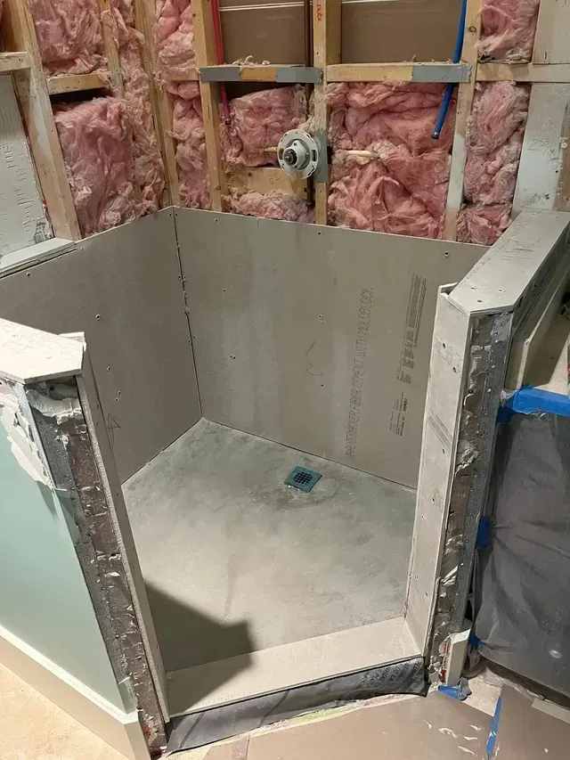 Partially tiled shower stall under construction with pink insulation and exposed wall studs