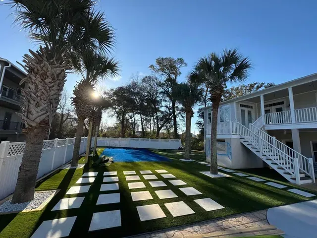 Sunlit palm-lined courtyard with grass, tiled walkway, and white apartment buildings