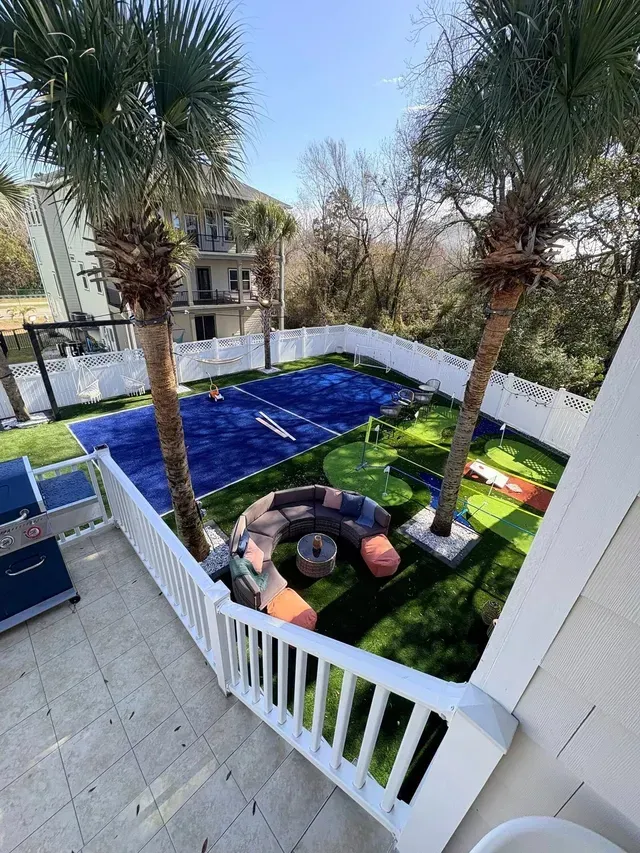 Backyard with blue tarp-covered area, lawn, palm trees, and an inflatable pool beside a white fence