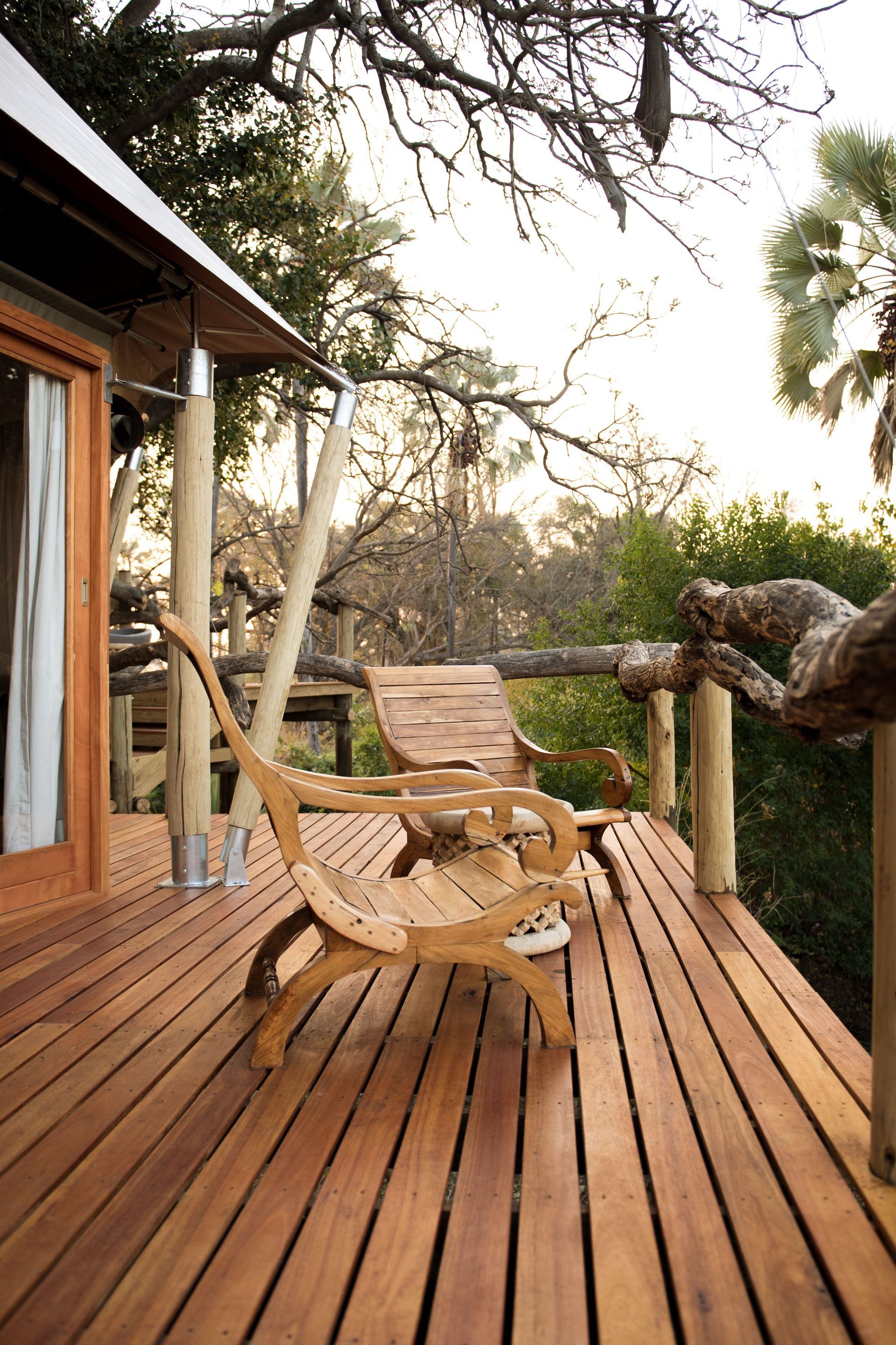 Wooden deck with lounge chairs beside a cabin, surrounded by trees at sunset.