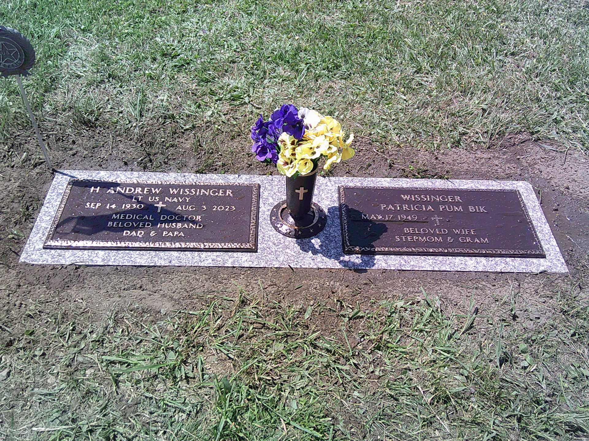 A grave with two plaques and a vase of flowers