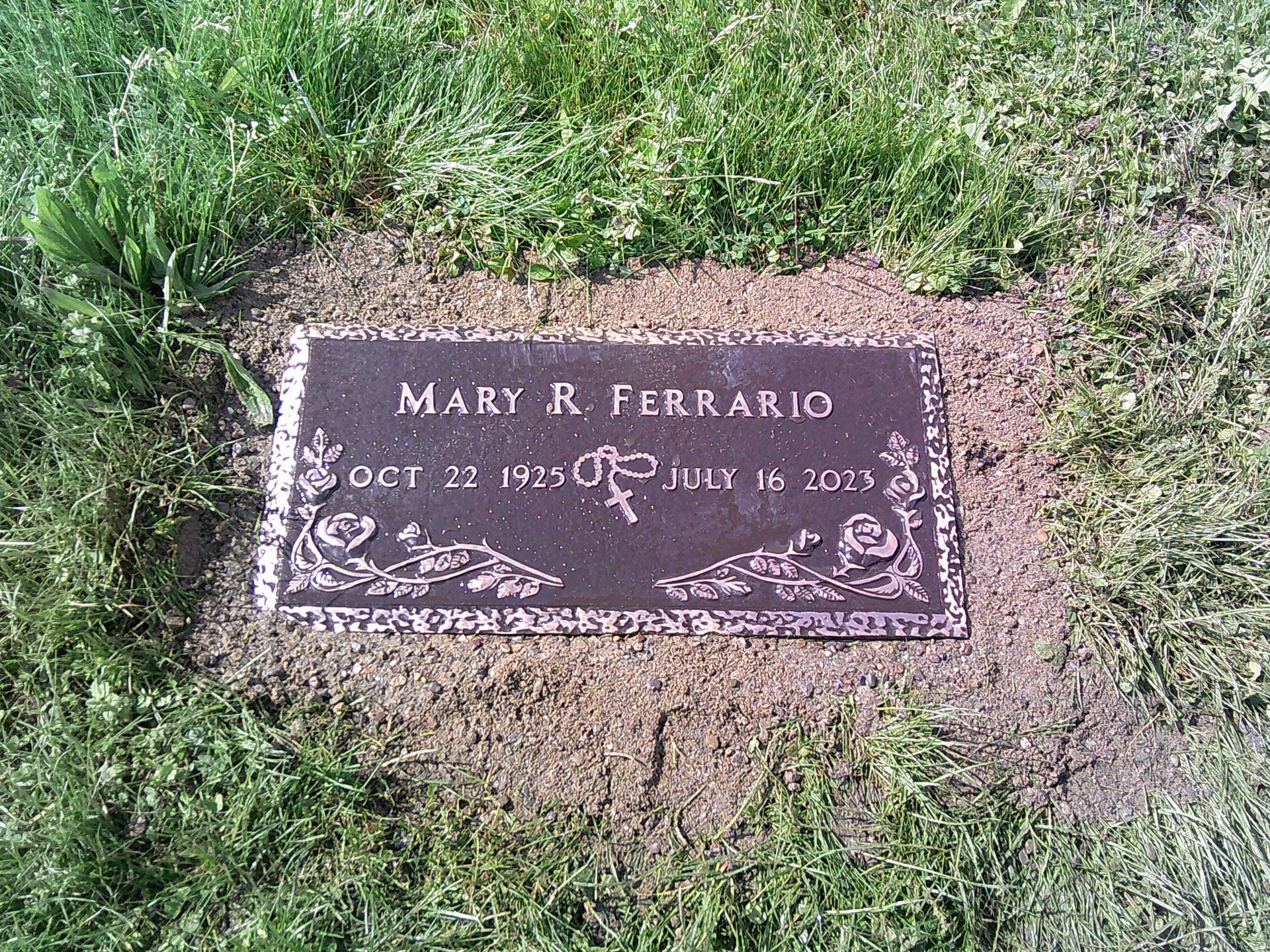 A gravestone for mary r. ferrario is sitting in the grass.