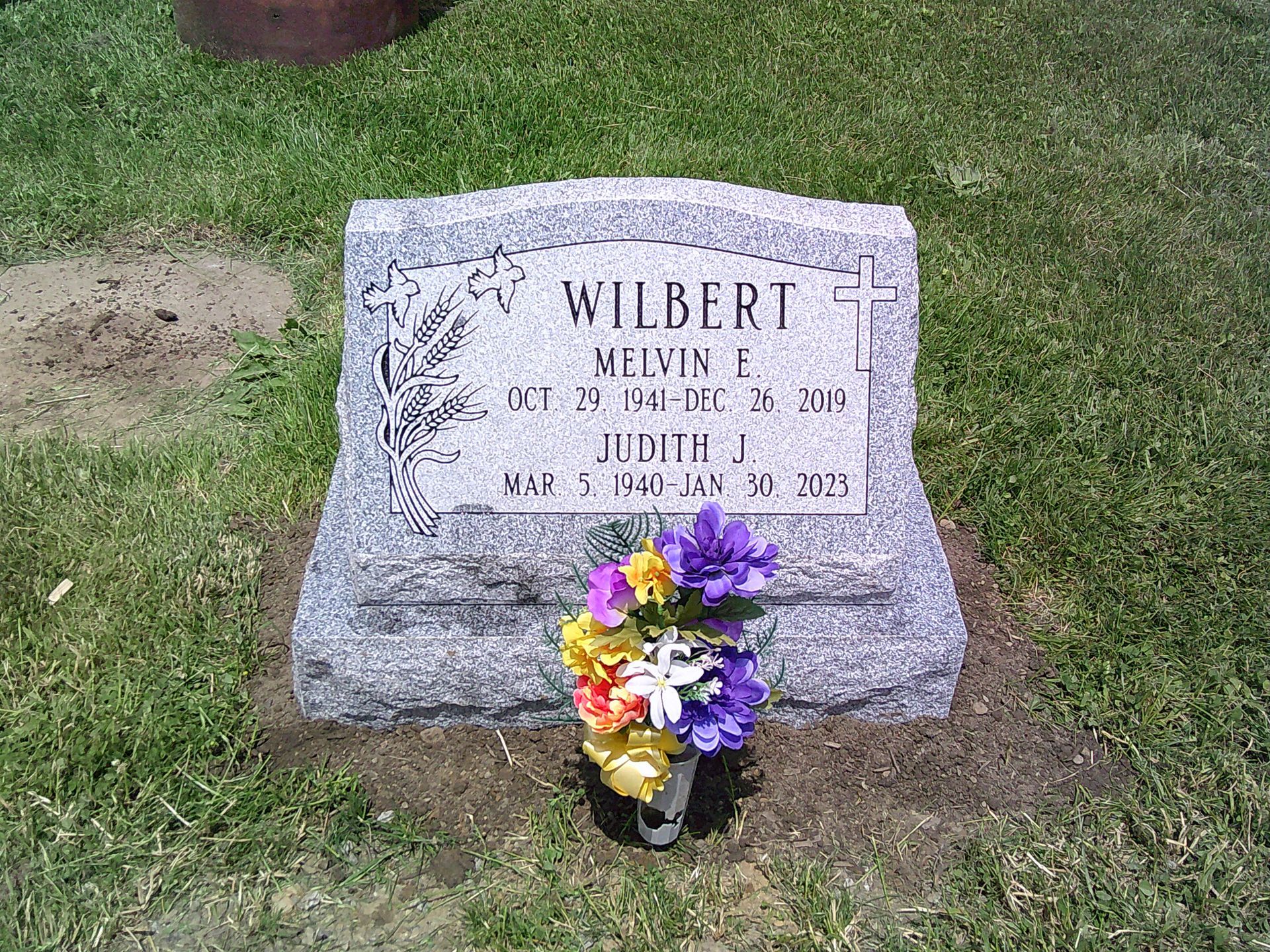 A gravestone for wilbert is in a cemetery with flowers in a vase.