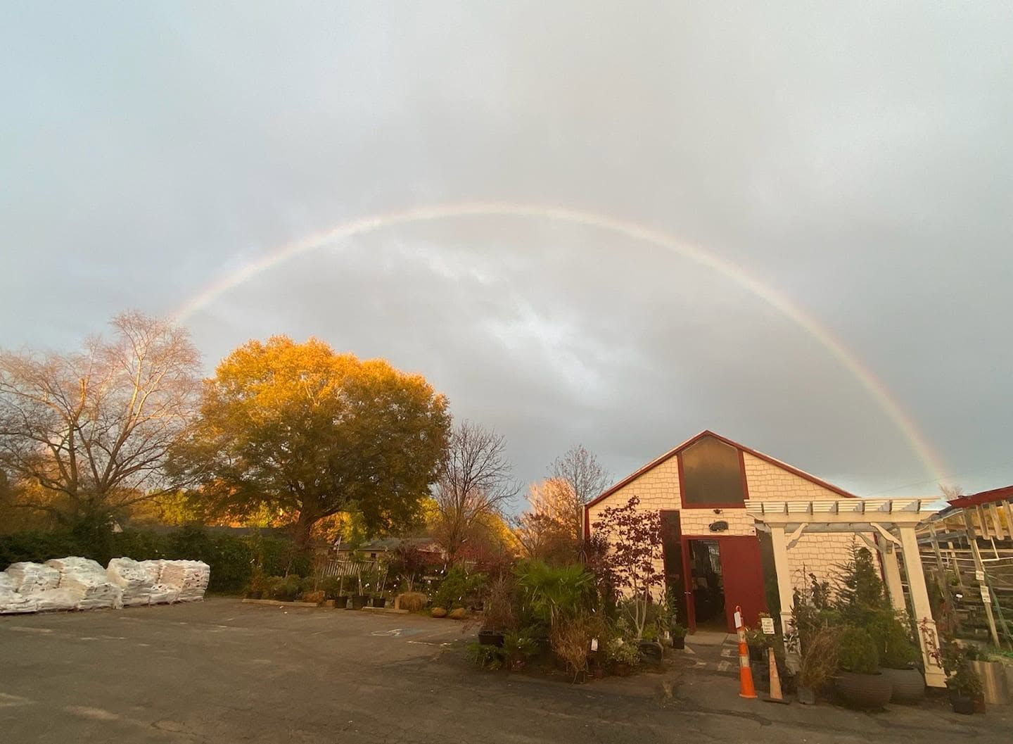 Rainbow over a rural building and autumn trees under a cloudy sky