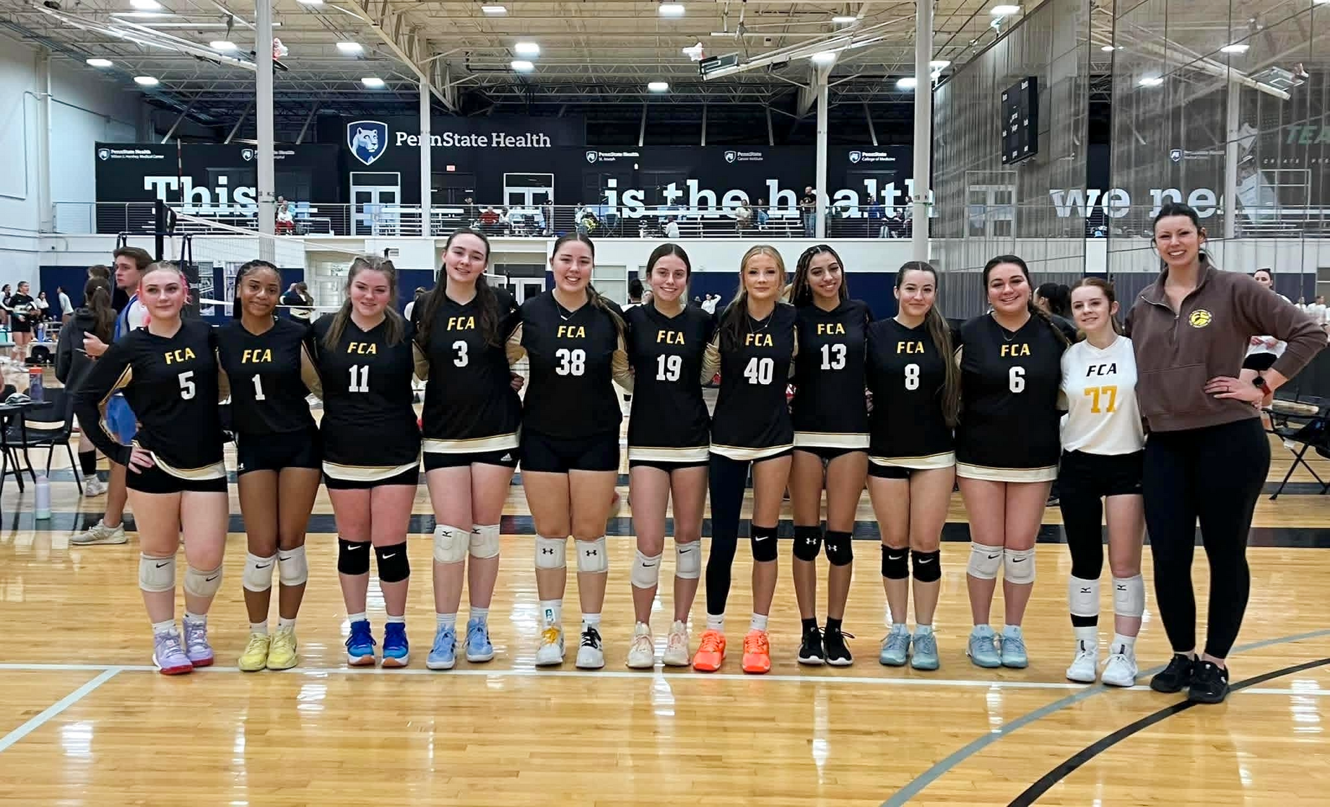 Volleyball team in teal jerseys posing for a group photo against a white backdrop