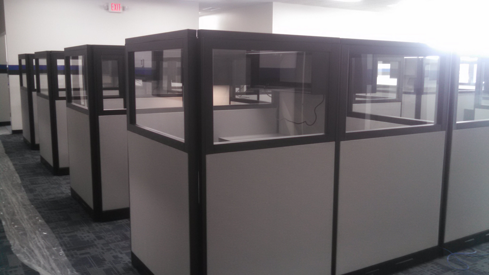 A row of cubicles in an office with an exit sign in the background