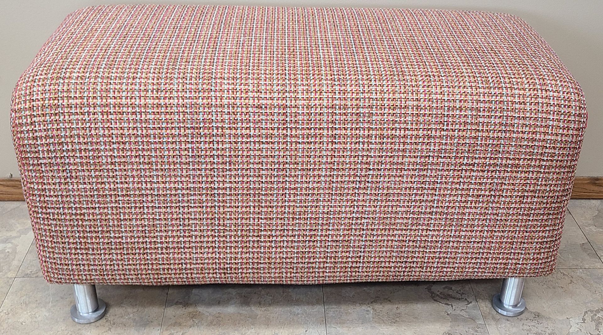 A pink ottoman is sitting on a concrete floor next to a wall.