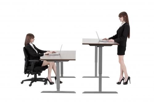 A woman is sitting at a desk and a woman is standing at a desk.