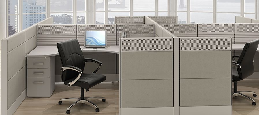 A cubicle in an office with a black chair and a laptop on the desk.