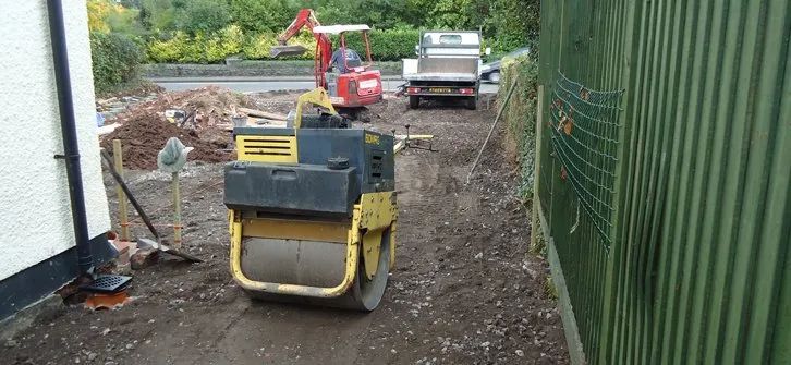 Urban Paving Bristol | A yellow and black roller is sitting on a dirt road next to a fence.