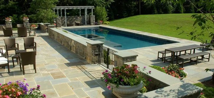 Urban Paving Bristol | A large swimming pool is surrounded by patio furniture and flowers.
