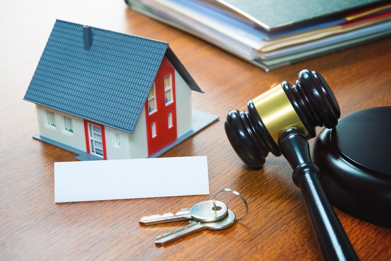A wooden table with a model house , keys and a judge 's gavel.