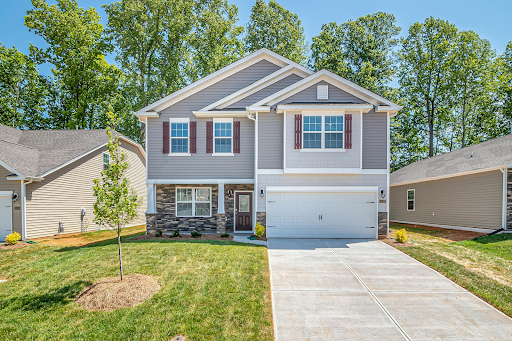 A large gray house with a white garage door is sitting on top of a lush green lawn.