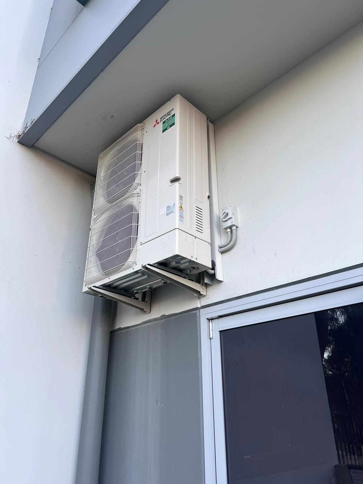 Wall-mounted outdoor air conditioner unit under an eave above a window