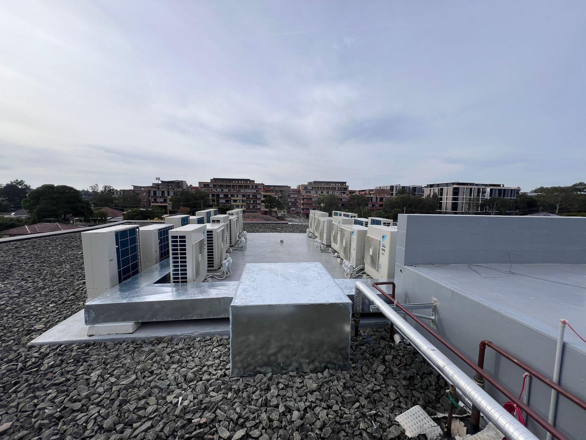 Rooftop HVAC units and metal ductwork on a gravel-covered roof under a cloudy sky