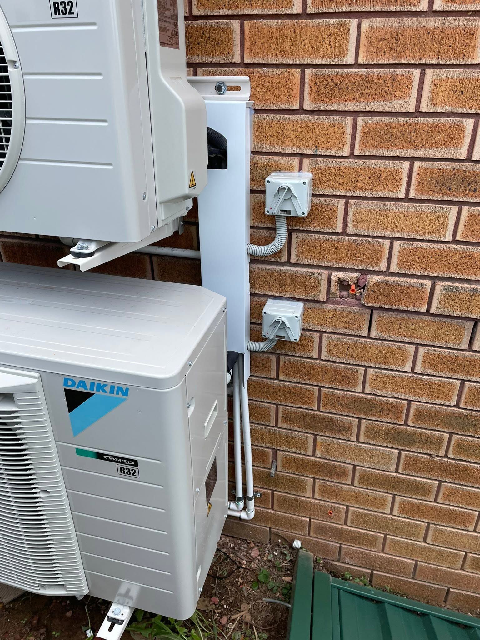 Outdoor air conditioning units mounted beside a brick house wall and electrical meter boxes