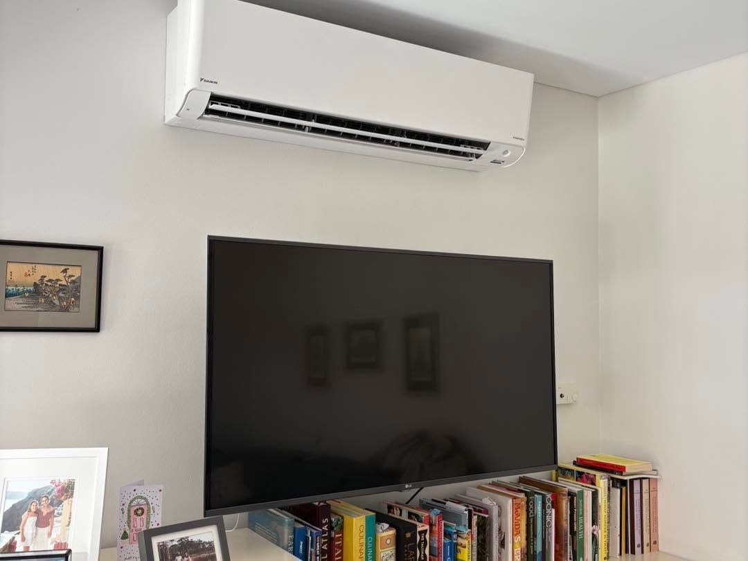Living room wall with a large TV, bookshelves below, framed art, and a wall-mounted air conditioner above