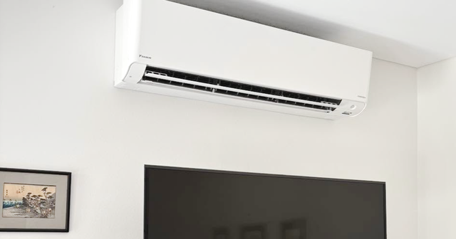 Wall-mounted white air conditioner above a black TV on a white wall
