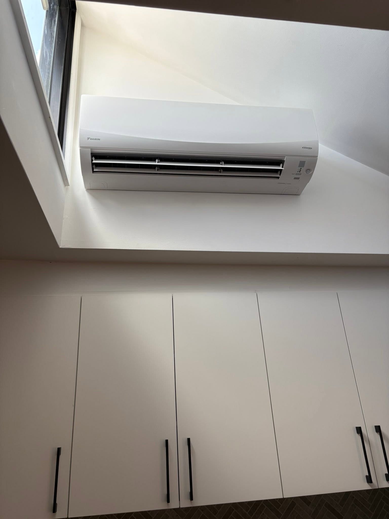 Wall-mounted air conditioner above white cabinets in a bright room with a slanted ceiling