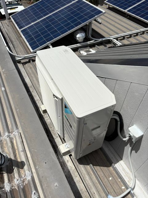 White outdoor electrical unit on a rooftop beside a solar panel and metal rails