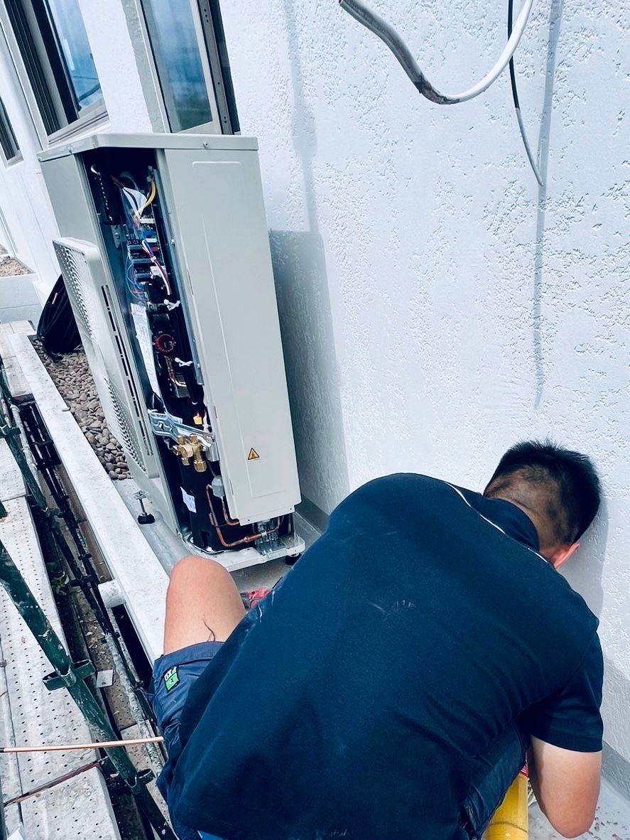 Technician working on an open electrical panel beside a ladder in a utility area