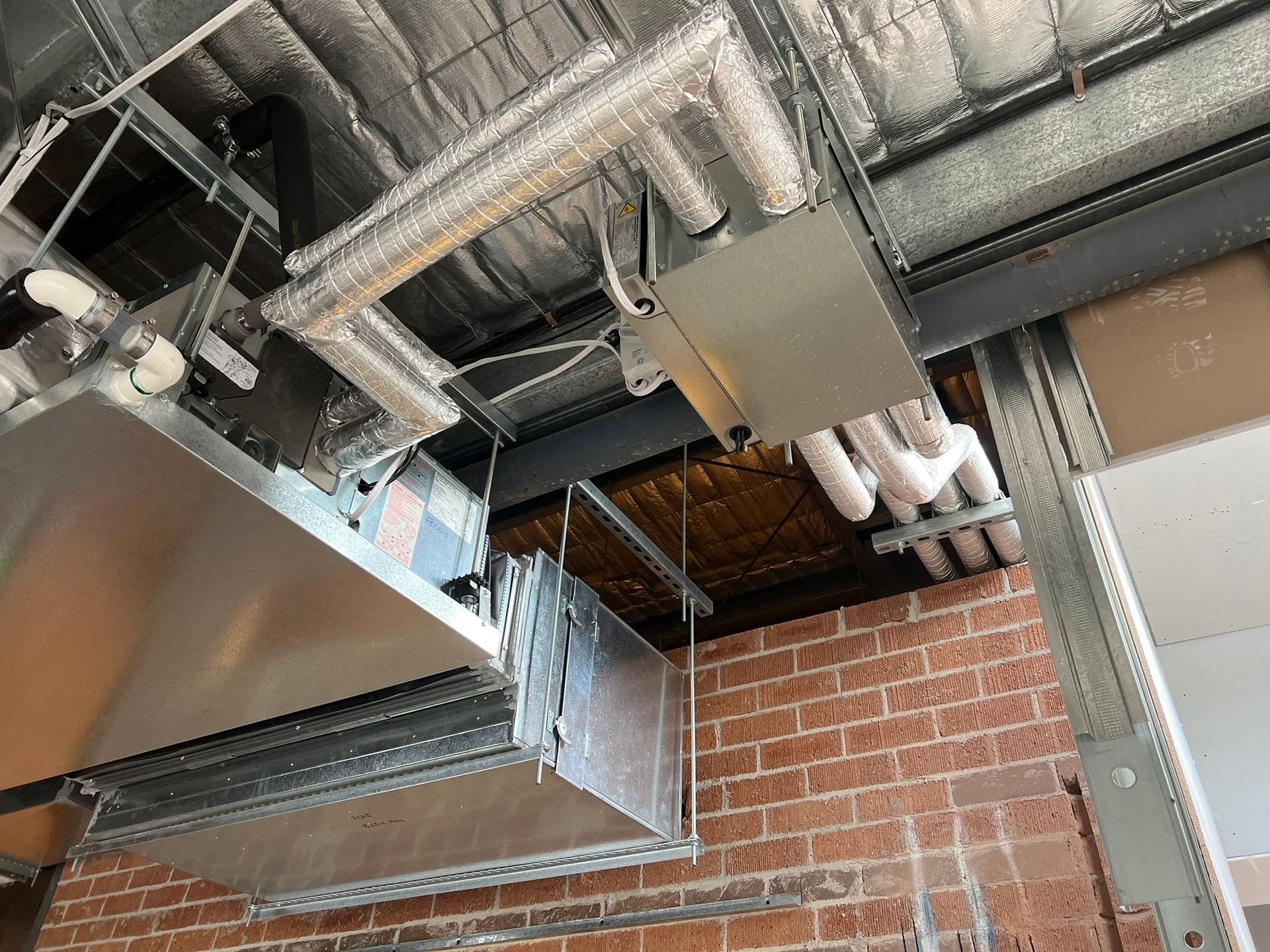 Exposed HVAC ducts and vents above a brick wall in an industrial interior ceiling.