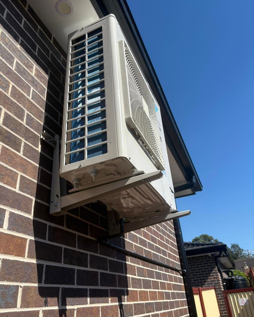 Wall-mounted air conditioner unit on a brick house exterior under a clear blue sky.