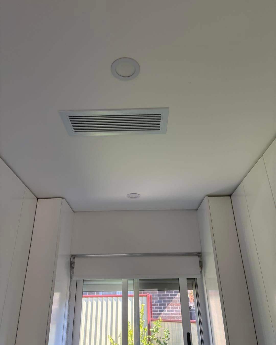 White hallway ceiling with vent and recessed light above a windowed doorway