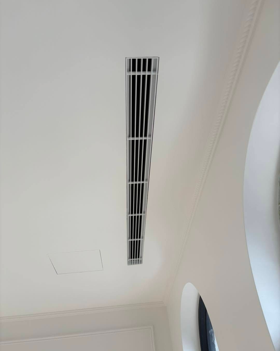 White ceiling with a long rectangular air vent and a curved light-colored wall edge