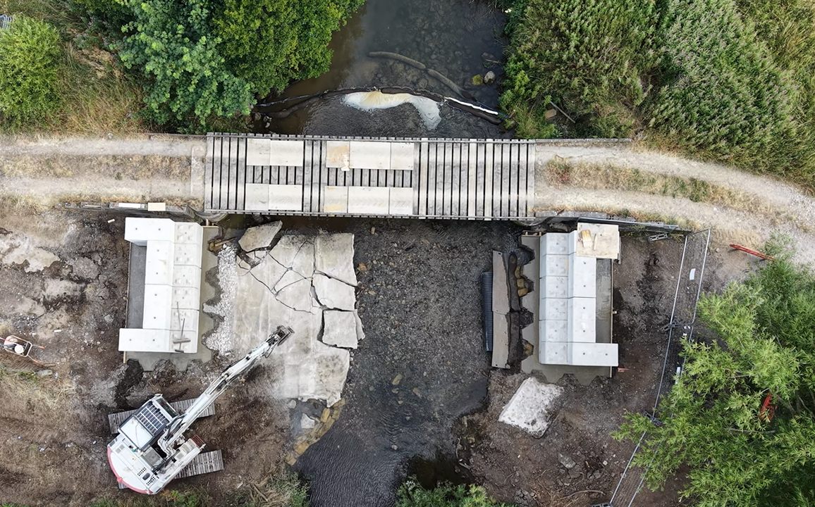 A digger breaking up the concrete on a stream bed to uncover the natural gravels.
