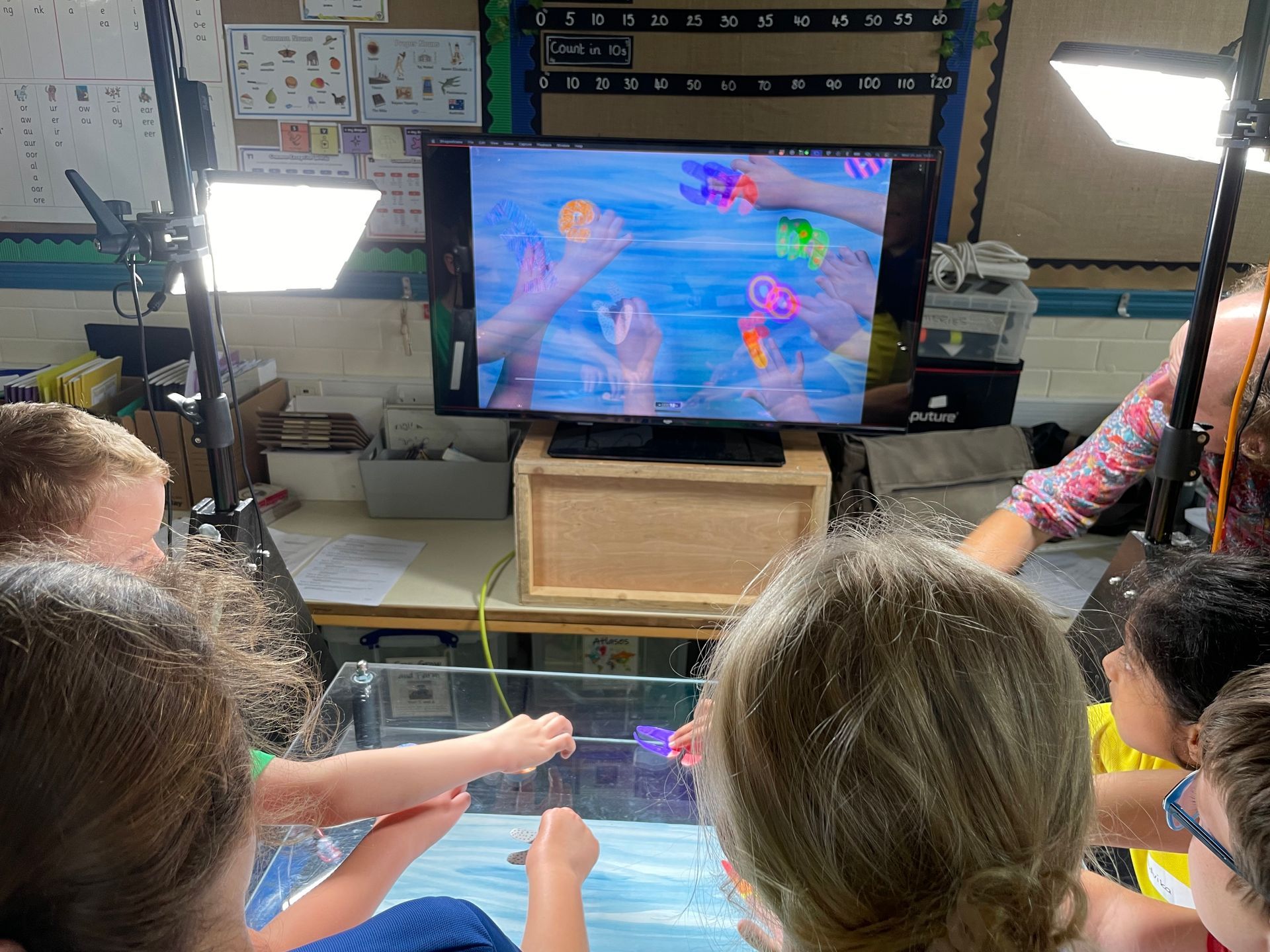 The backs of several children's heads as they watch and engage with an interactive screen.
