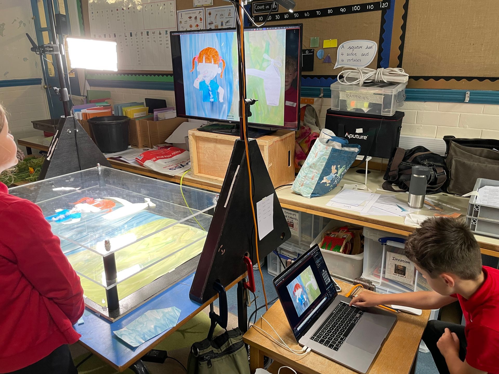 Children working in a classroom making a stop-motion animation film on two screens and a transparent table where they are filming it.