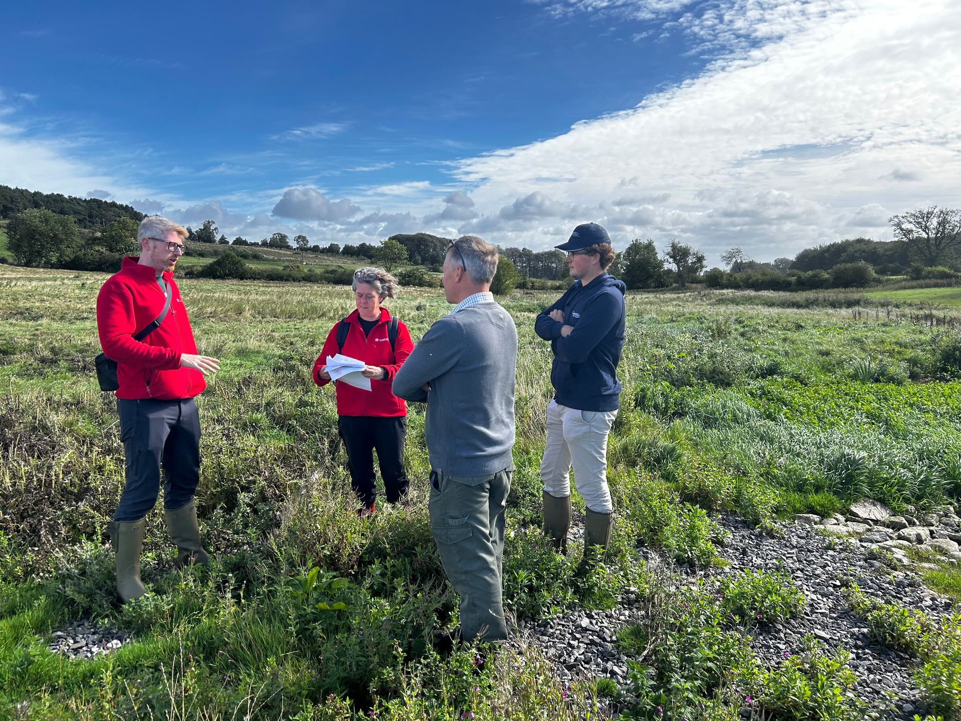 Four people stood in a wetland talking to each other and facing inwards.