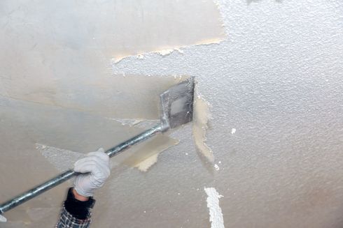 Person uses a paint roller on a beige ceiling and wall corner, touching up peeling paint.