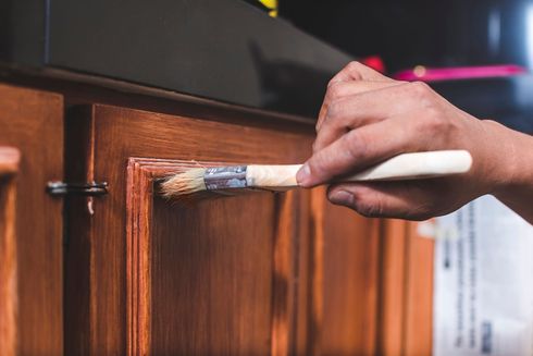 Hand painting a wooden cabinet with a white brush handle