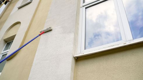 Paint roller on a blue pole reaching the exterior wall of a building near a window